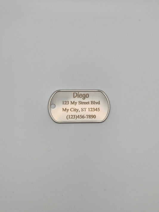 Aluminum military ID-style dog tag with engraved name, full address, and phone number sitting on a gray background