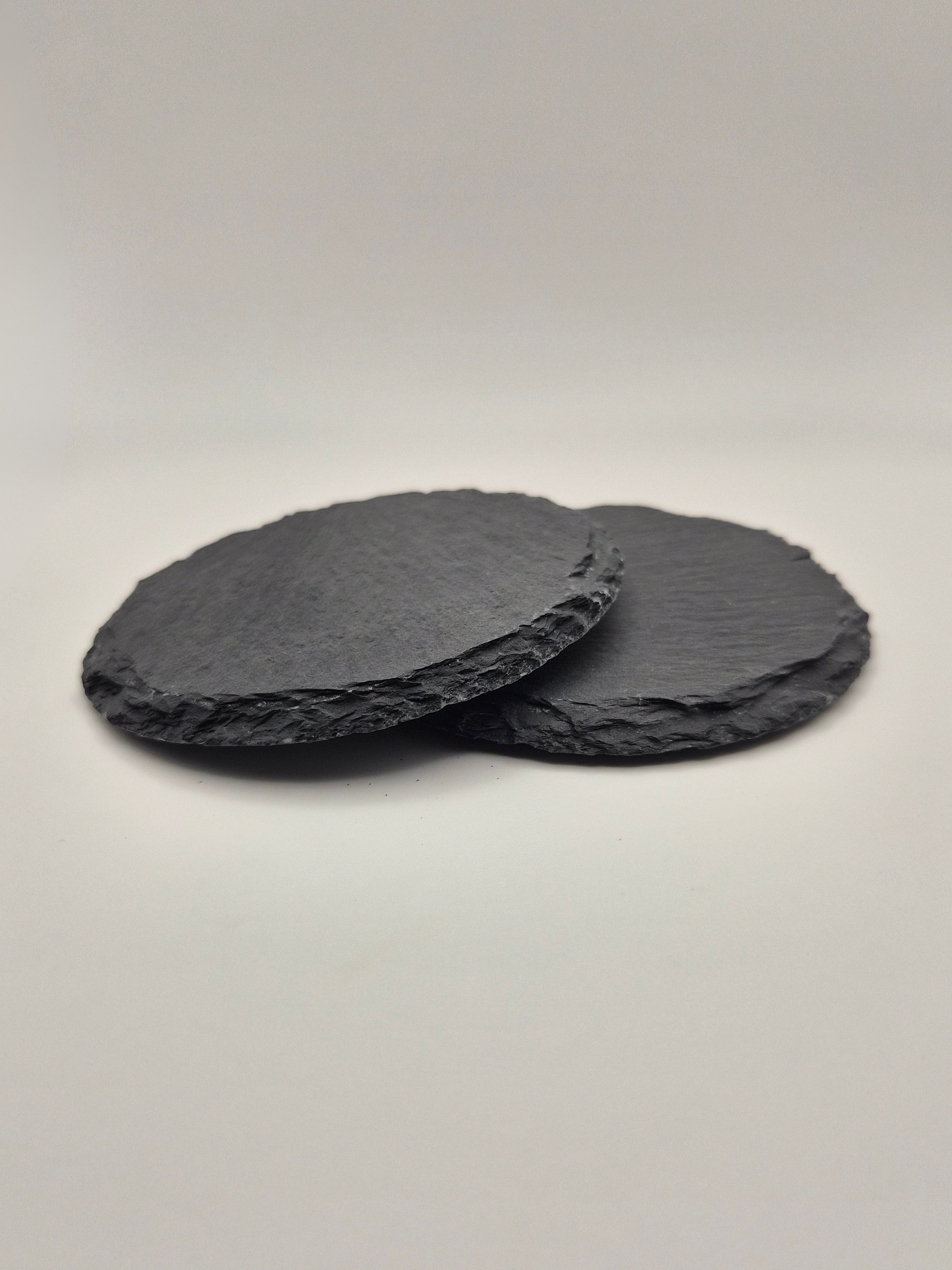 Two round slate coasters, stacked so that you can see the side thickness and texture on a light background