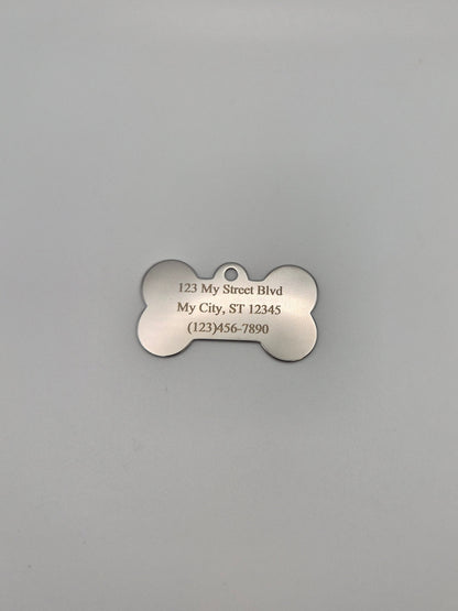 Stainless steel, bone-shaped dog tag with engraved full address and phone number on a gray background