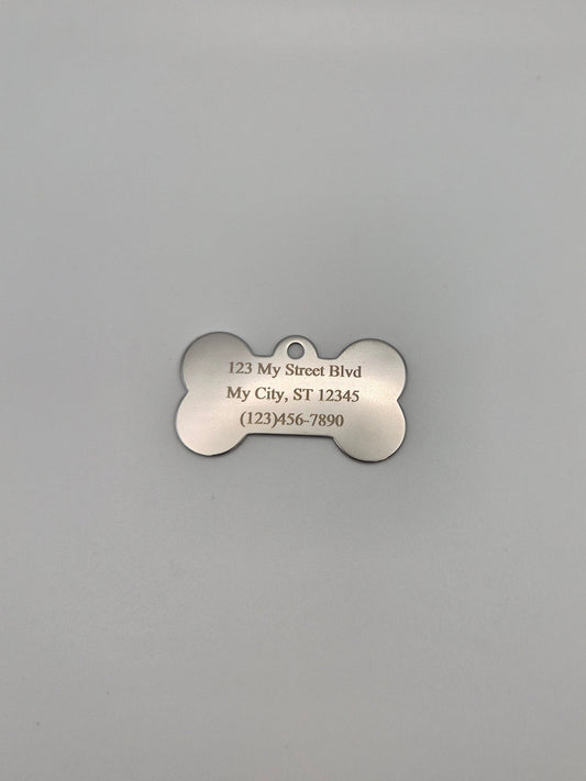 Stainless steel, bone-shaped dog tag with engraved full address and phone number on a gray background