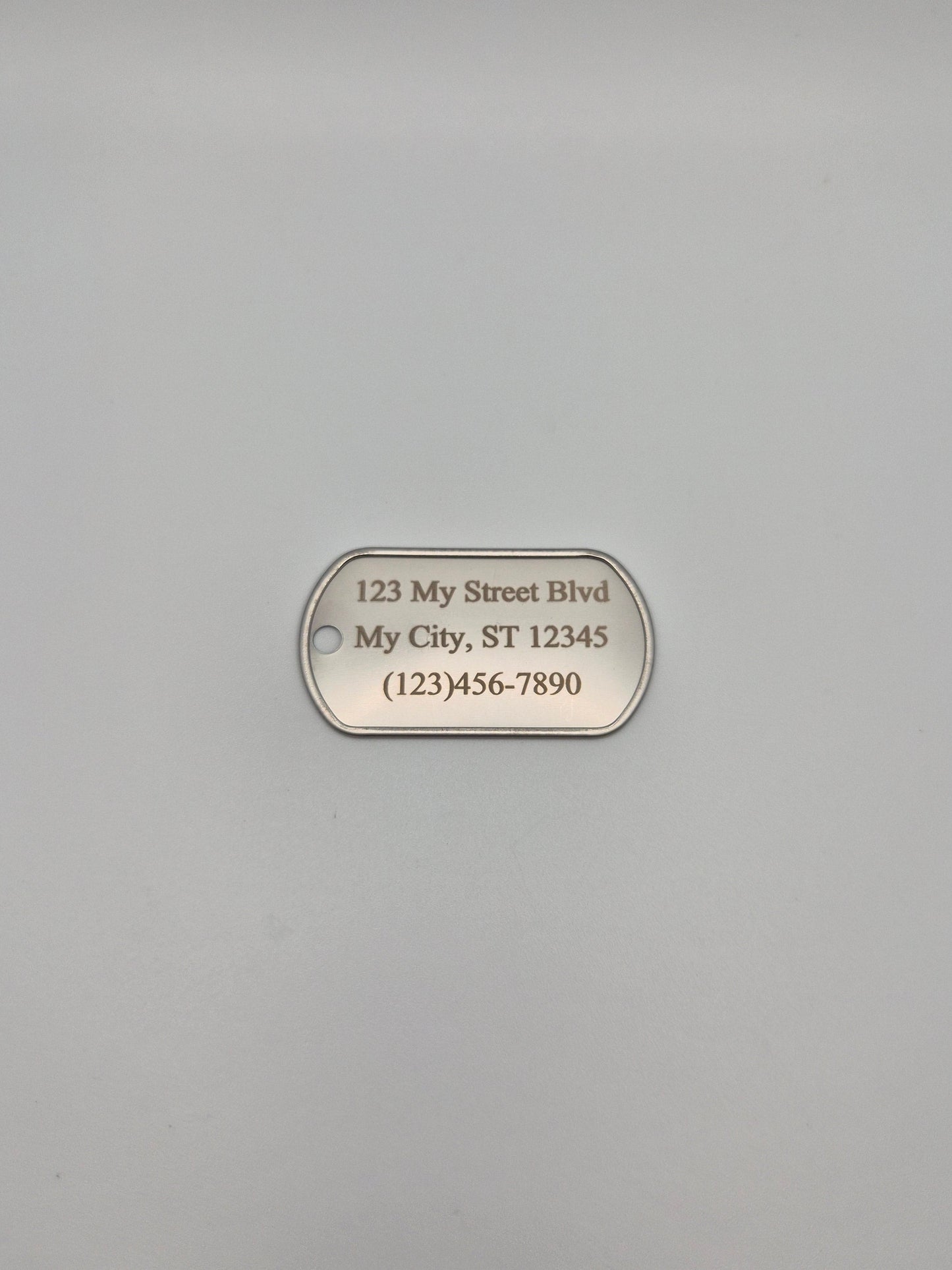 Aluminum, military ID-style dog tag with  full street address & phone number sitting on a gray background