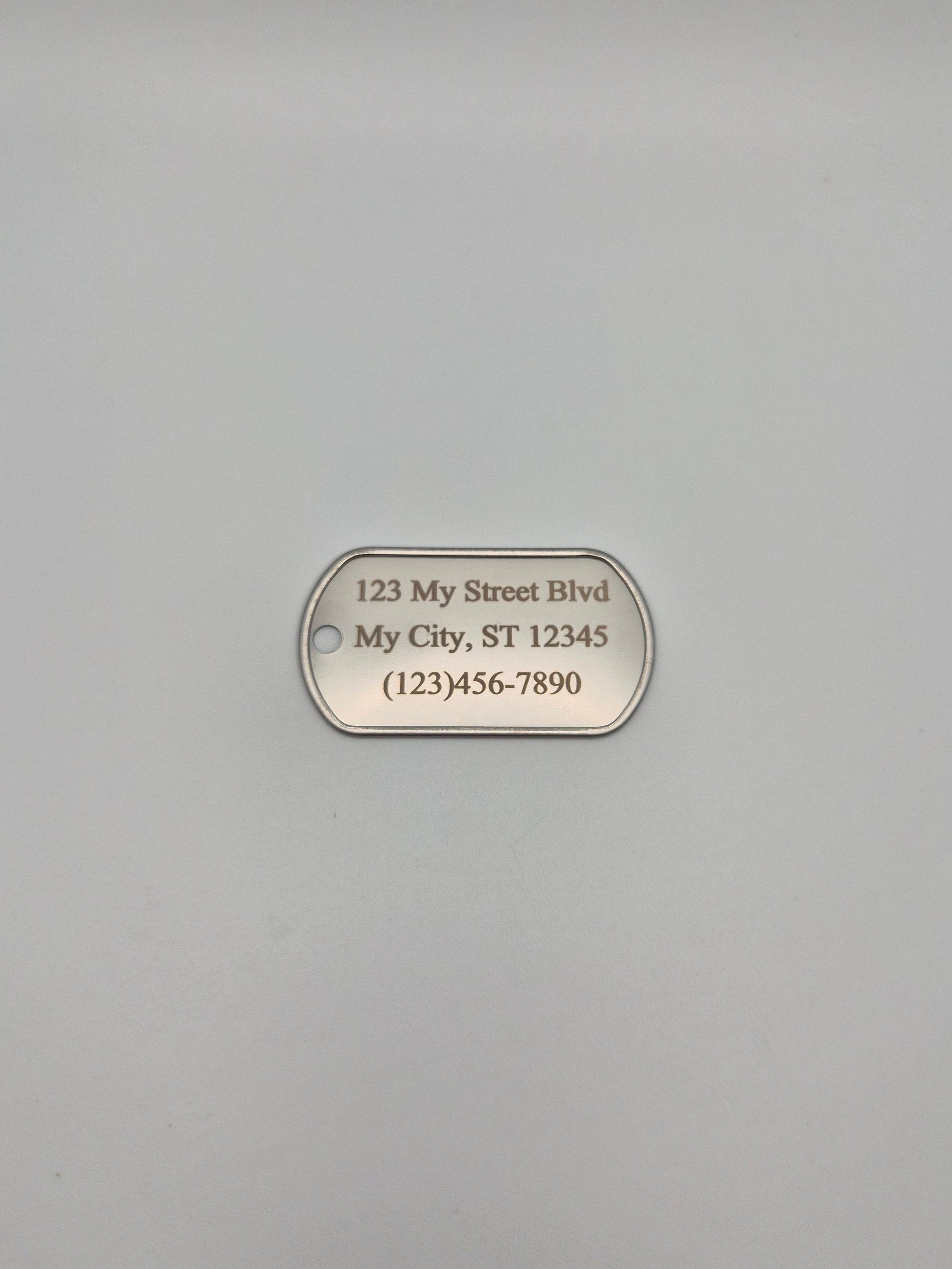 Aluminum, military ID-style dog tag with  full street address & phone number sitting on a gray background