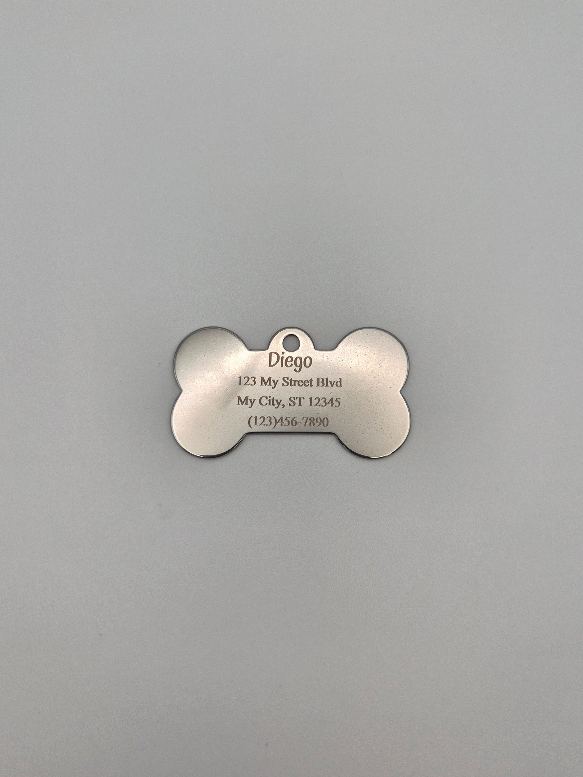 Stainless steel, bone-shaped dog tag with 4 lines of engraved text on a gray background