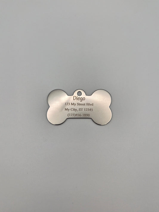 Stainless steel, bone-shaped dog tag with 4 lines of engraved text on a gray background