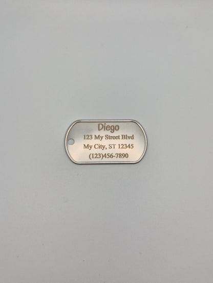 Aluminum military ID-style dog tag with engraved name, full address, and phone number sitting on a gray background