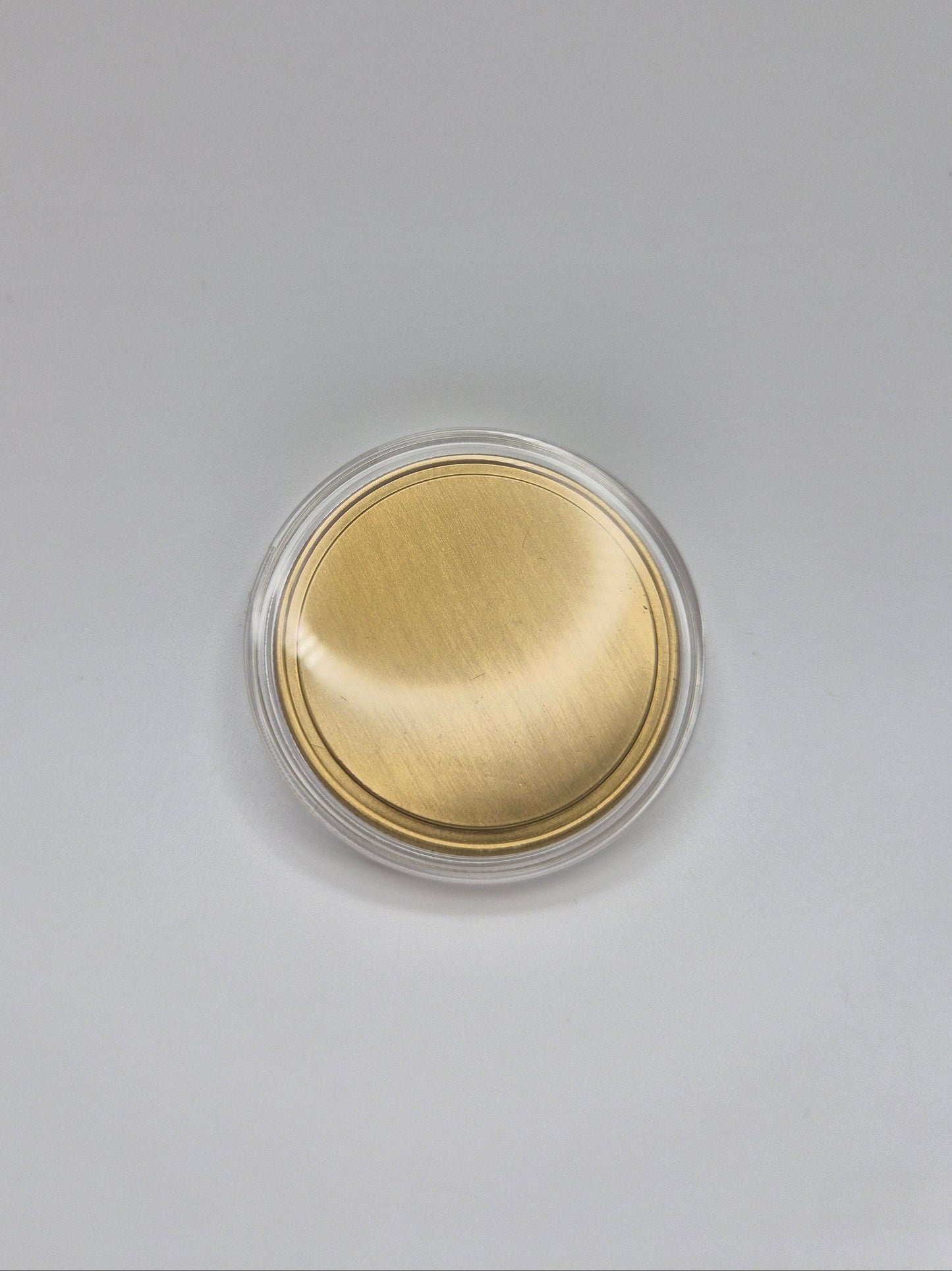Gold, blank commemorative coin inside it's clear plastic protective cover on a light background
