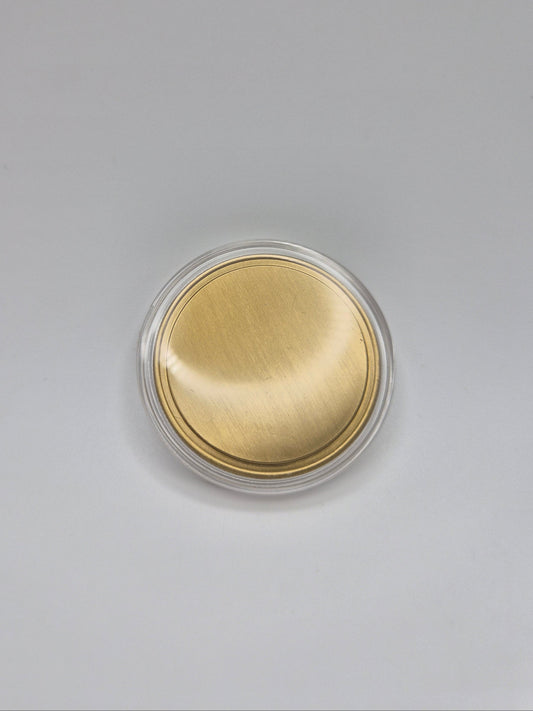 Gold, blank commemorative coin inside it's clear plastic protective cover on a light background