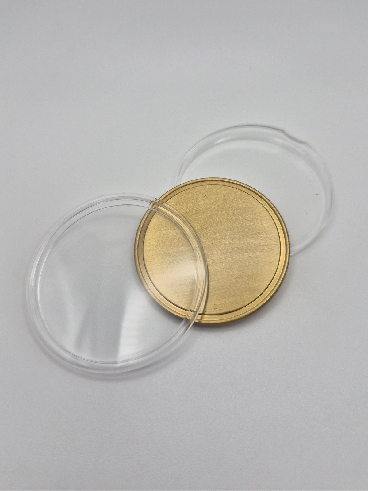 Gold, blank commemorative coin with clear plastic protective cover open on a light background