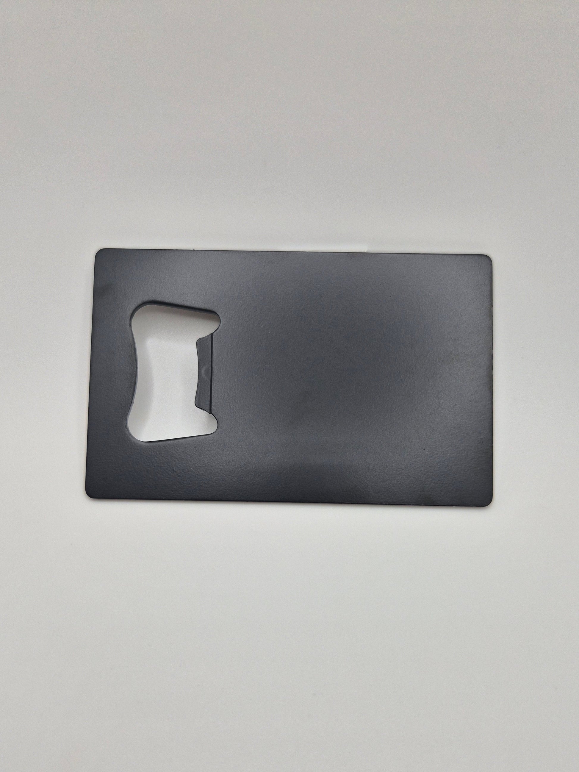 Credit card-sized, stainless steel bottle opener with a matte black finish on a light background