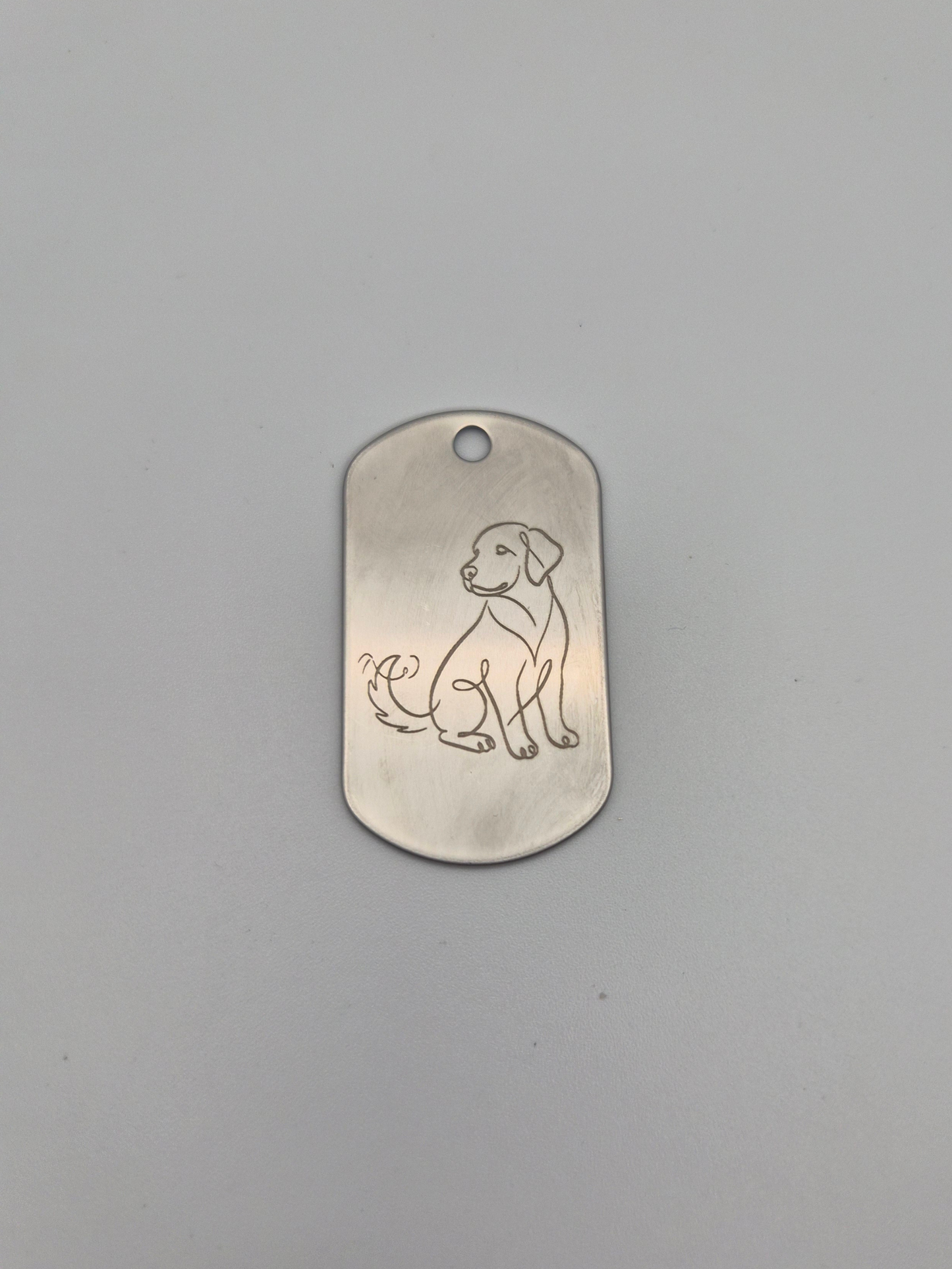 Aluminum military ID-style dog tag with an engraved dog design on a gray background