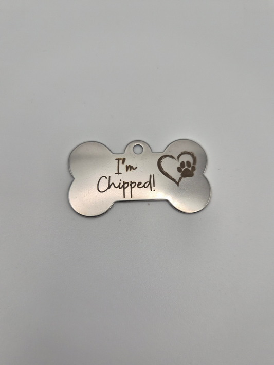 Stainless steel bone-shaped dog tag with 'I'm Chipped!' text and a heart-paw engraved on it sitting on a light background