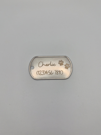 Metal dog tag with 2 engraved pawprints, the name 'Charlie,' and phone number on a gray background