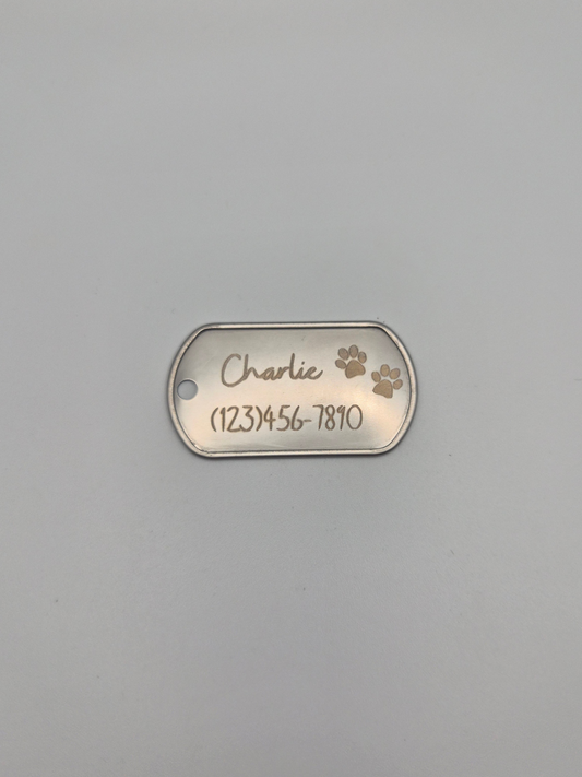 Metal dog tag with 2 engraved pawprints, the name 'Charlie,' and phone number on a gray background