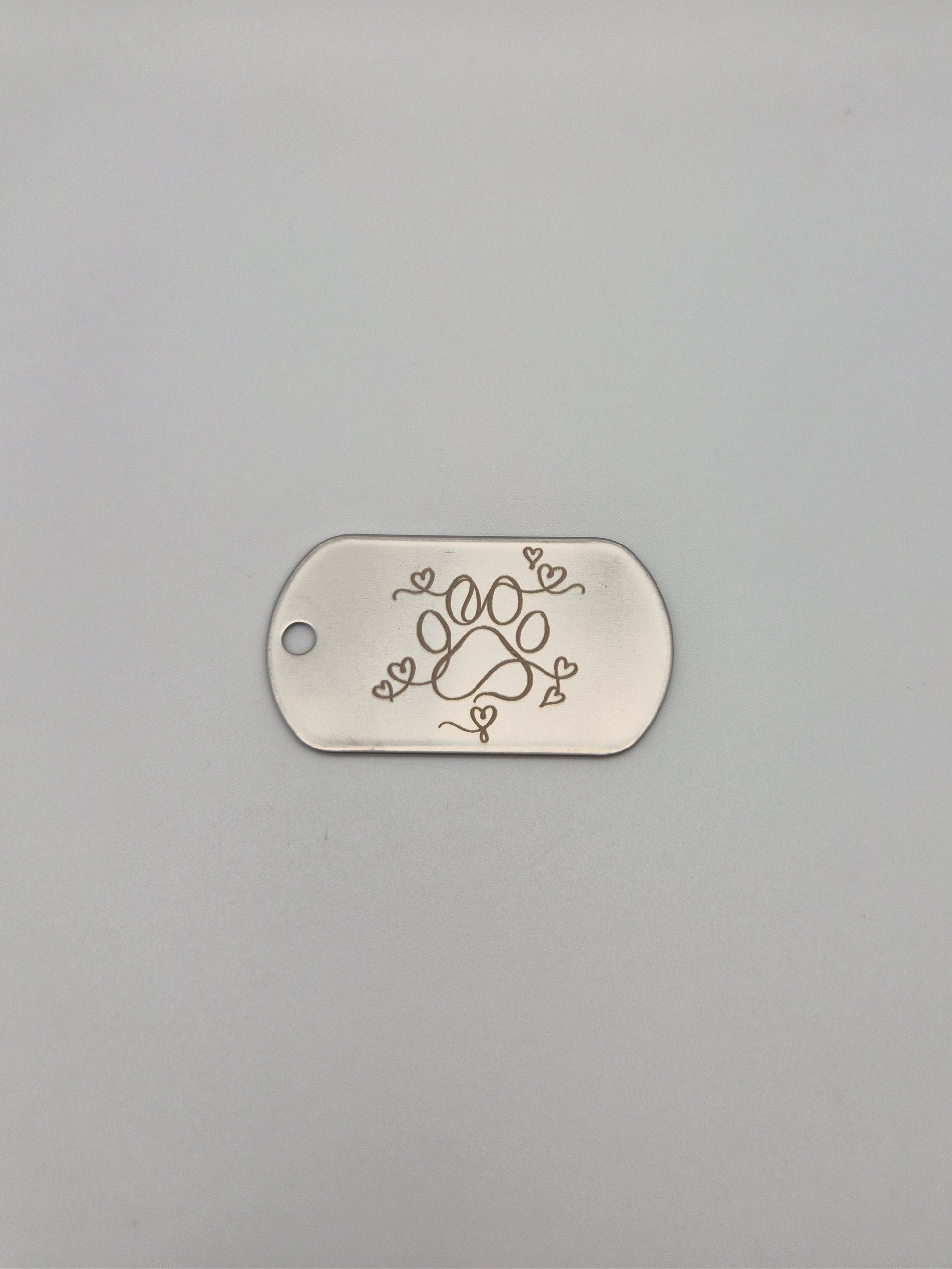 Aluminum, military ID-style dog tag with engraved paw & hearts design on a gray background