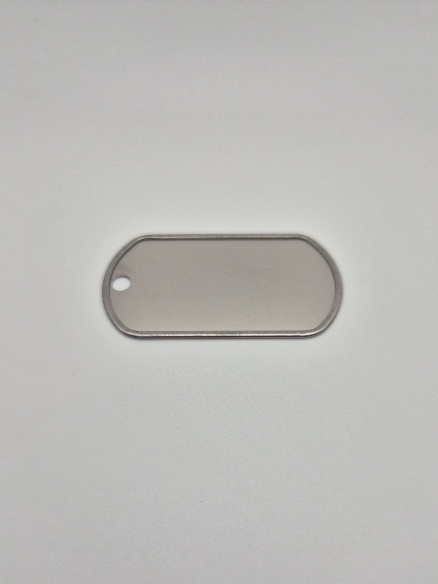 Back side, with a rolled edge, of an aluminum, military id-style dog tag on a light background