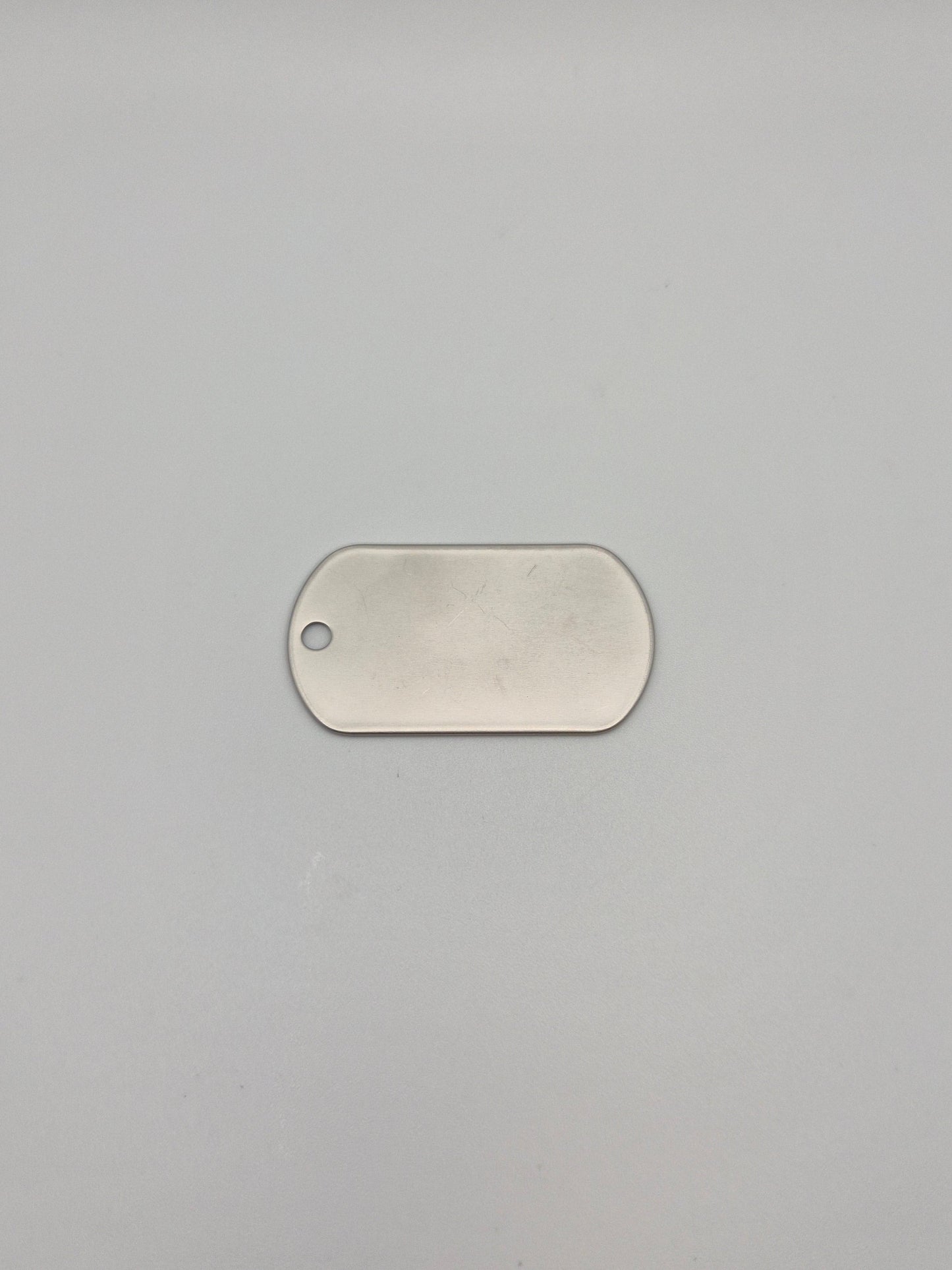 Front, smooth side of an aluminum, military id-style dog tag on a light background