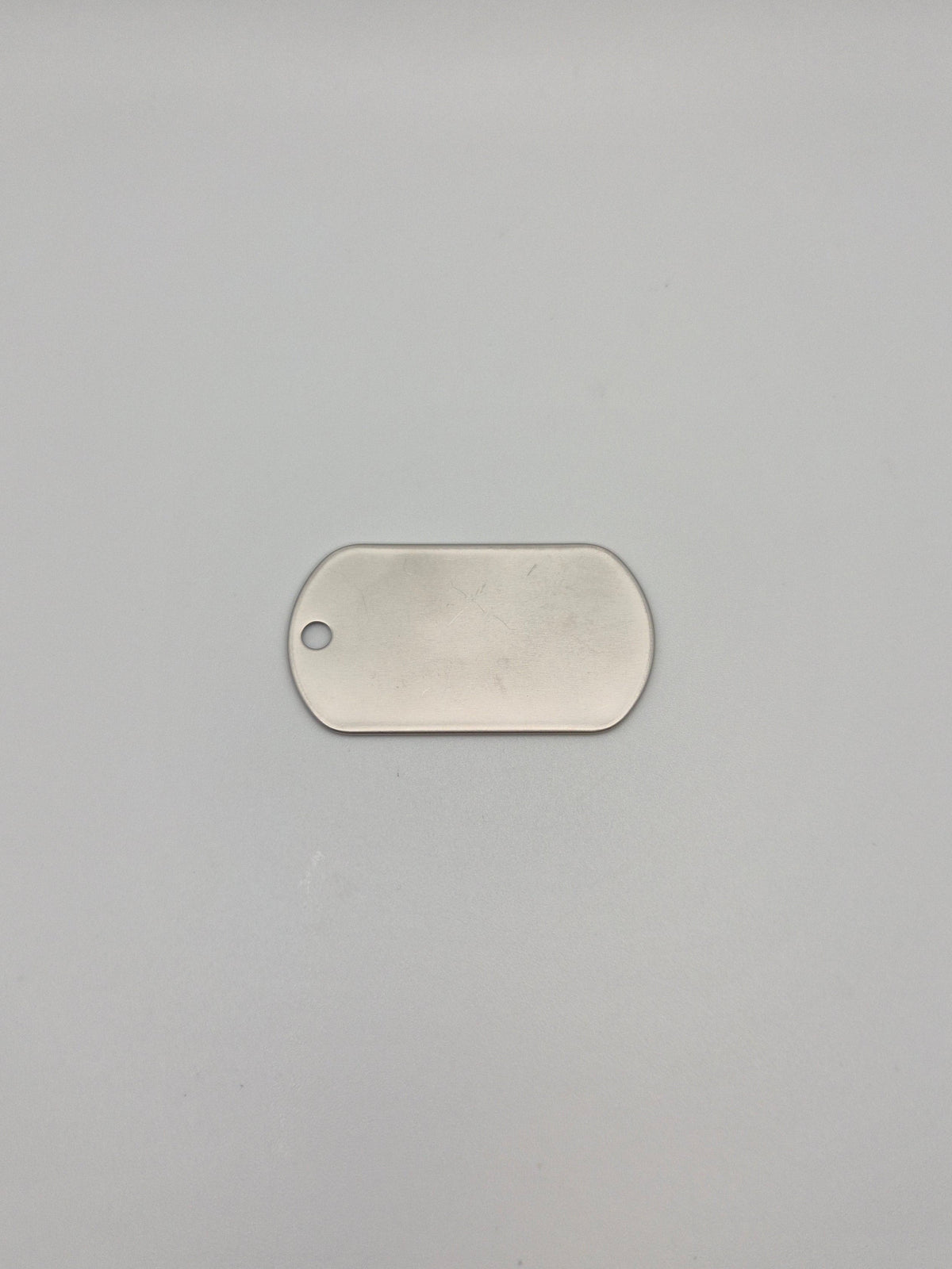 Front, smooth side of an aluminum, military id-style dog tag on a light background