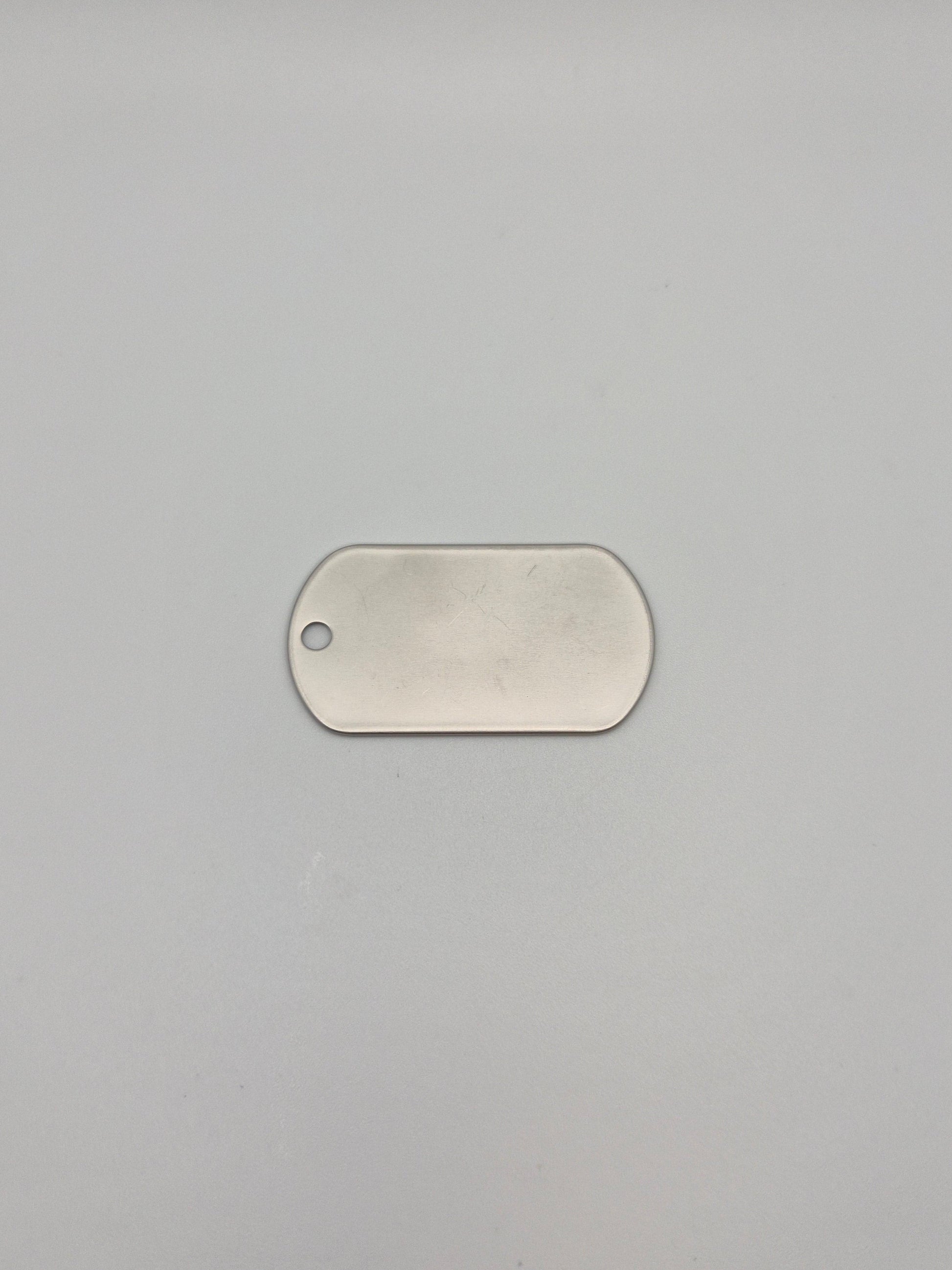 Front, smooth side of an aluminum, military id-style dog tag on a light background