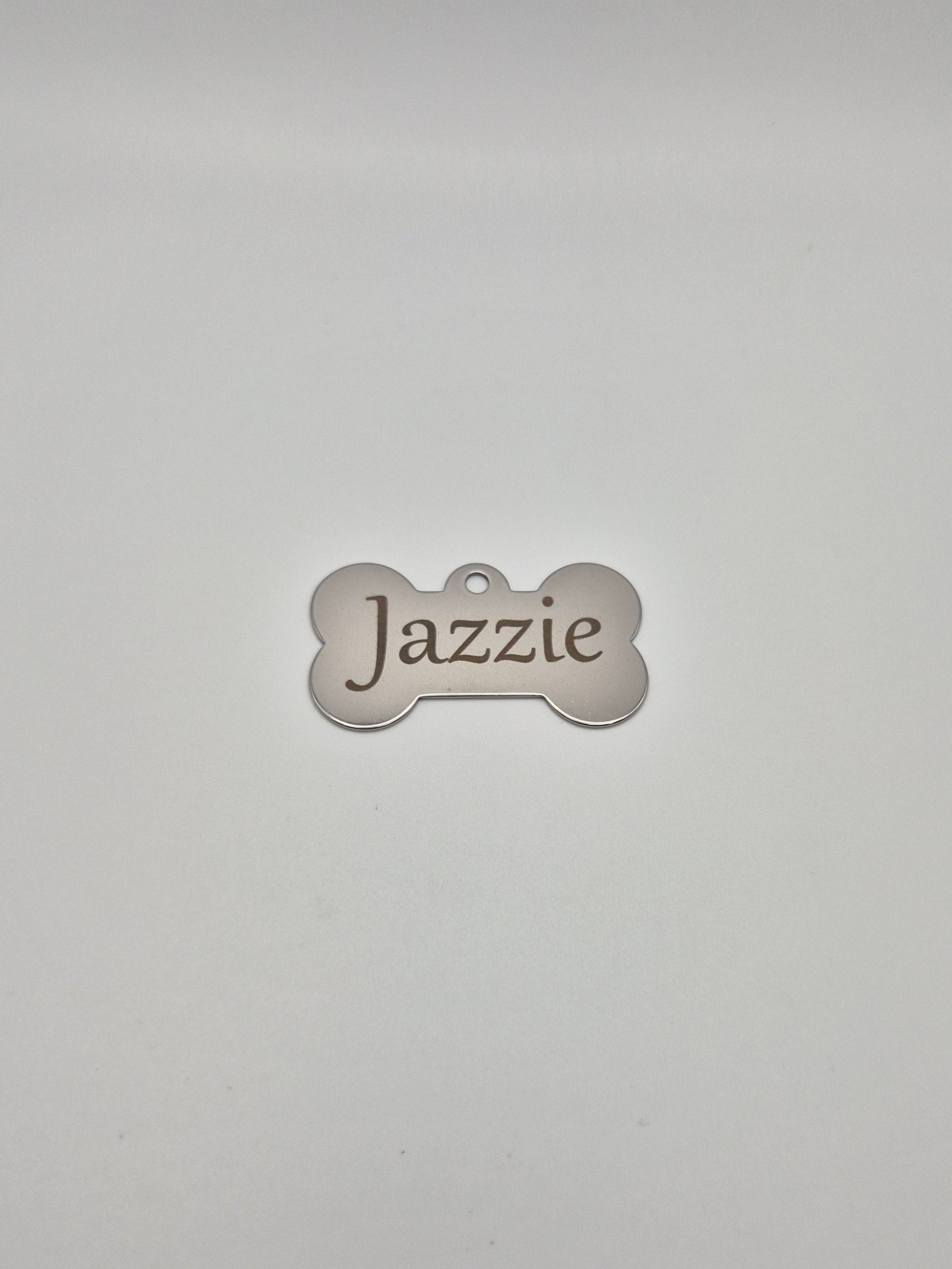 Stainless steel, bone-shaped dog tag with 'Jazzie' engraved on it, sitting on a light gray background