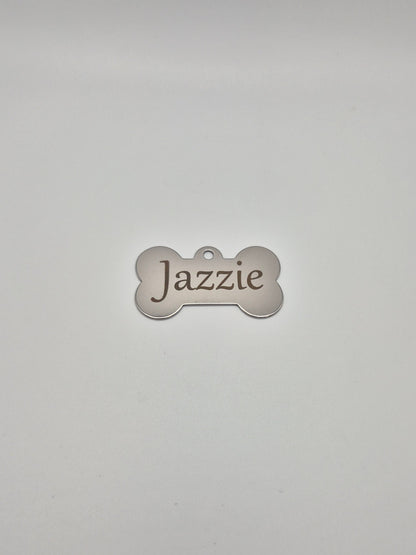 Stainless steel, bone-shaped dog tag with 'Jazzie' engraved on it, sitting on a light gray background