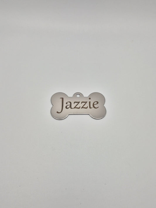 Stainless steel, bone-shaped dog tag with 'Jazzie' engraved on it, sitting on a light gray background