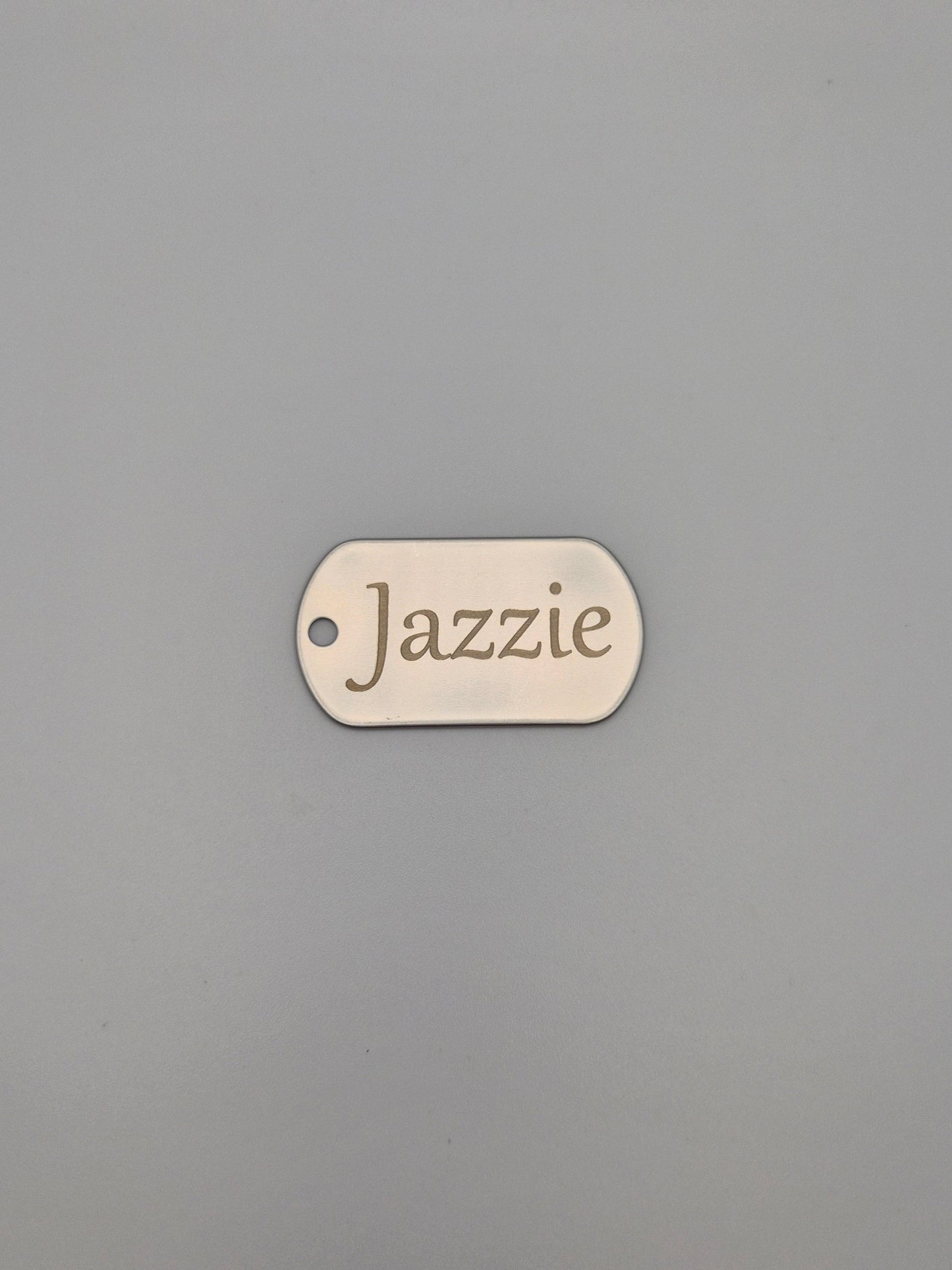 Aluminum, military ID-style dog tag with 'Jazzie' engraved on a gray background