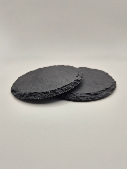 Two round slate coasters, stacked so that you can see the side thickness and texture on a light background