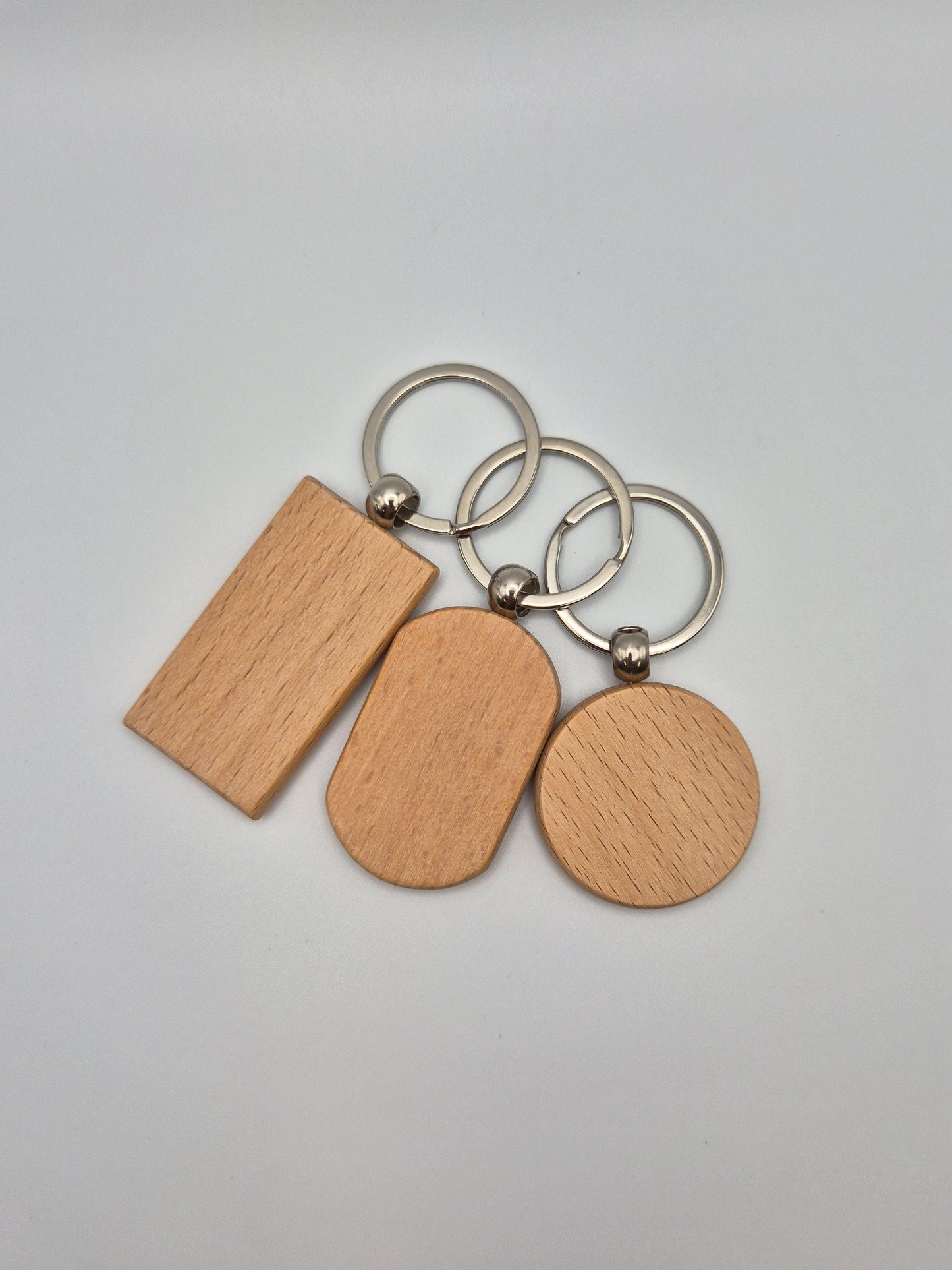 Three wooden keychains, rectangular, oval, and round, with metal rings sitting on a light gray background
