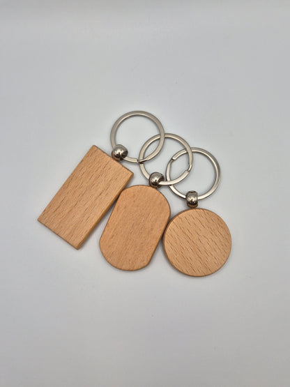 Three wooden keychains, rectangular, oval, and round, with metal rings sitting on a light gray background