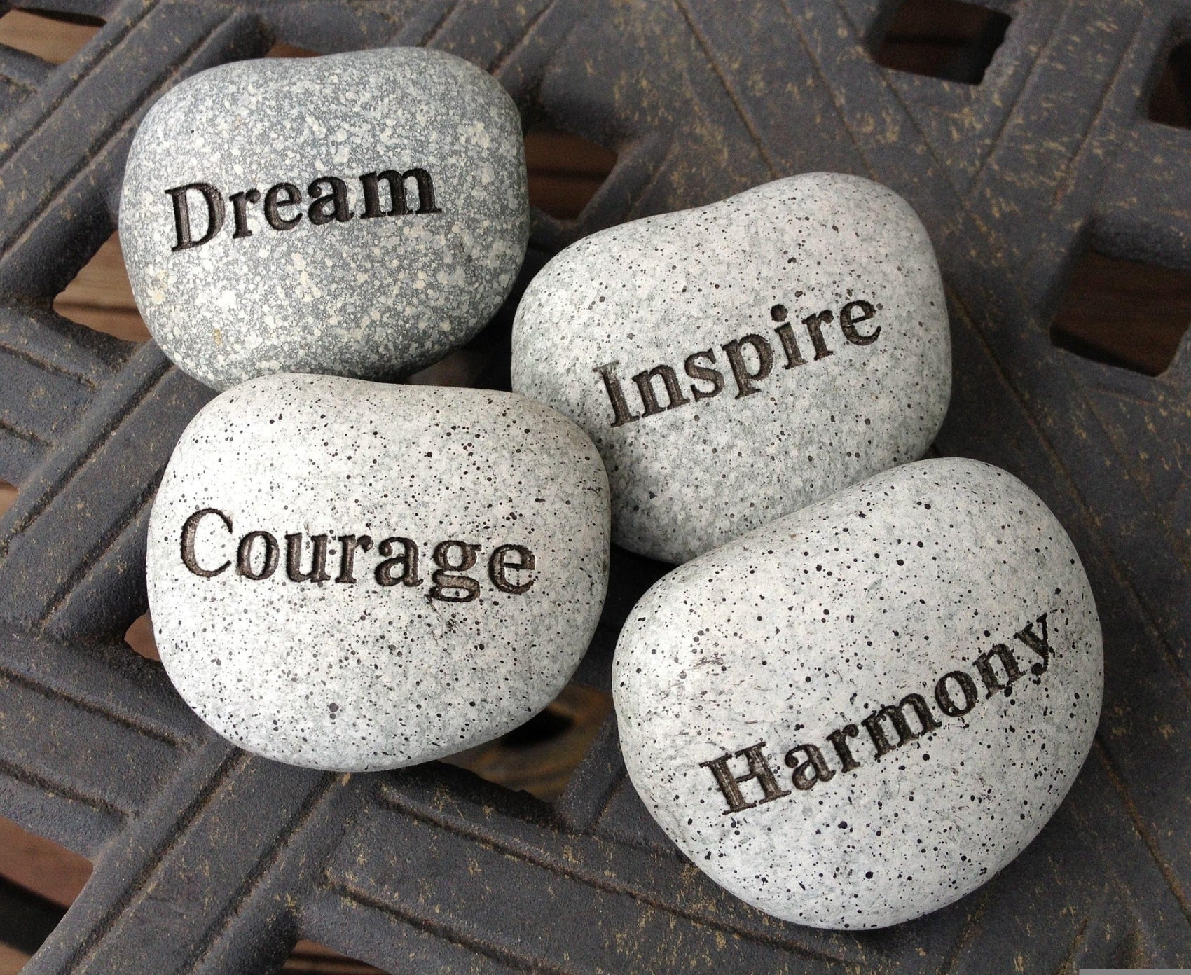 Four smooth, light-colored river stones with words "Dream", "Inspire", "Courage" and "Harmony" engraved on them